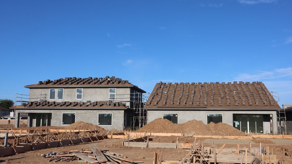 Two newly constructed houses with scaffolding under a clear blue sky.